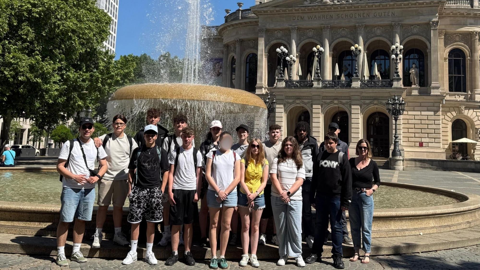 Gruppe von Jugendlichen vor einem Brunnen auf einem Platz in Frankfurt mit der Alten Oper im Hintergrund.