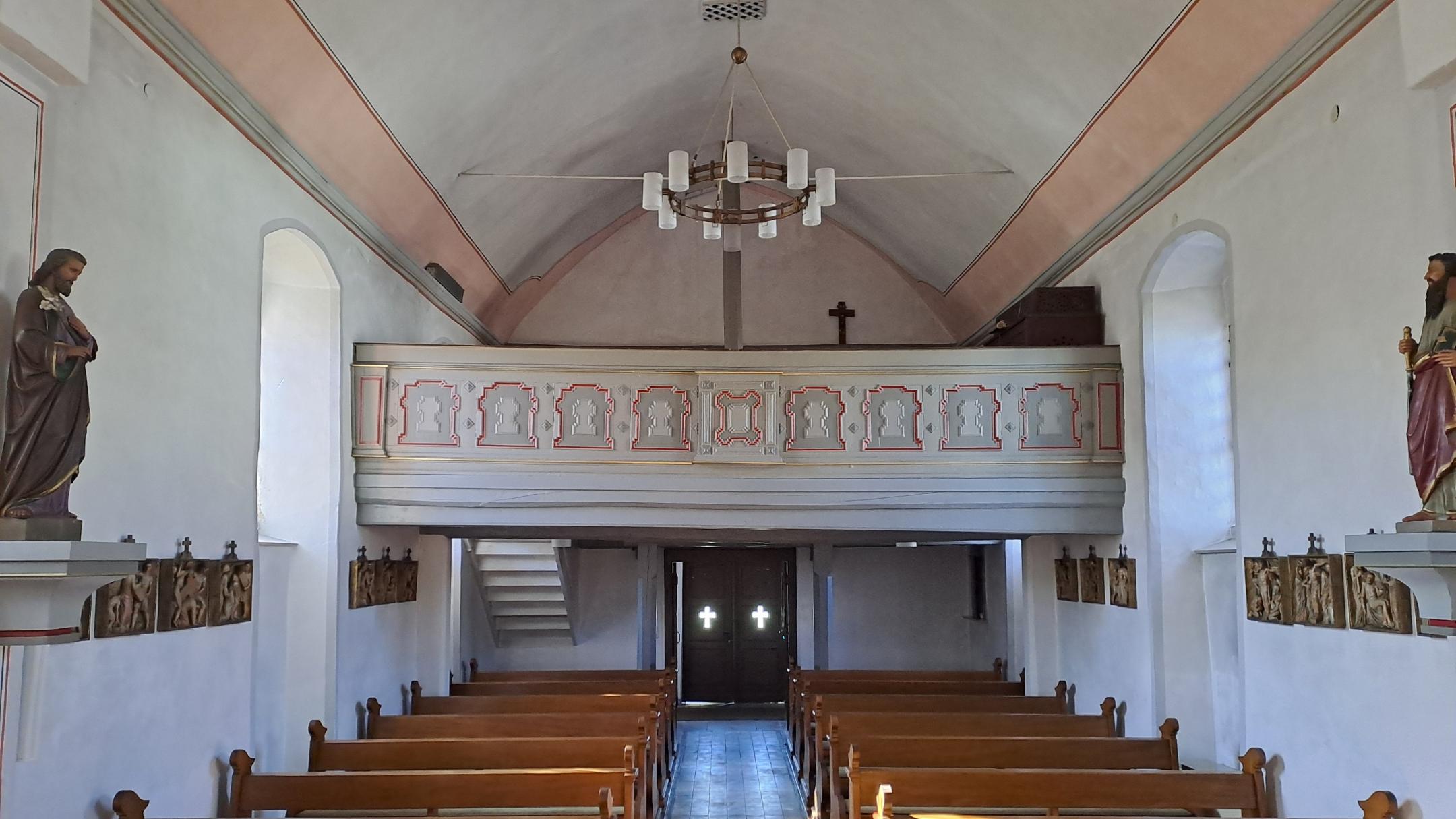 Blick vom Altar durch das Kirchenschiff der Kirche St. Matthias in Richtung Eingang. Holzbänke stehen in mehreren Reihen. Am hinteren Ende befindet sich die Empore über dem Eingangsbereich.