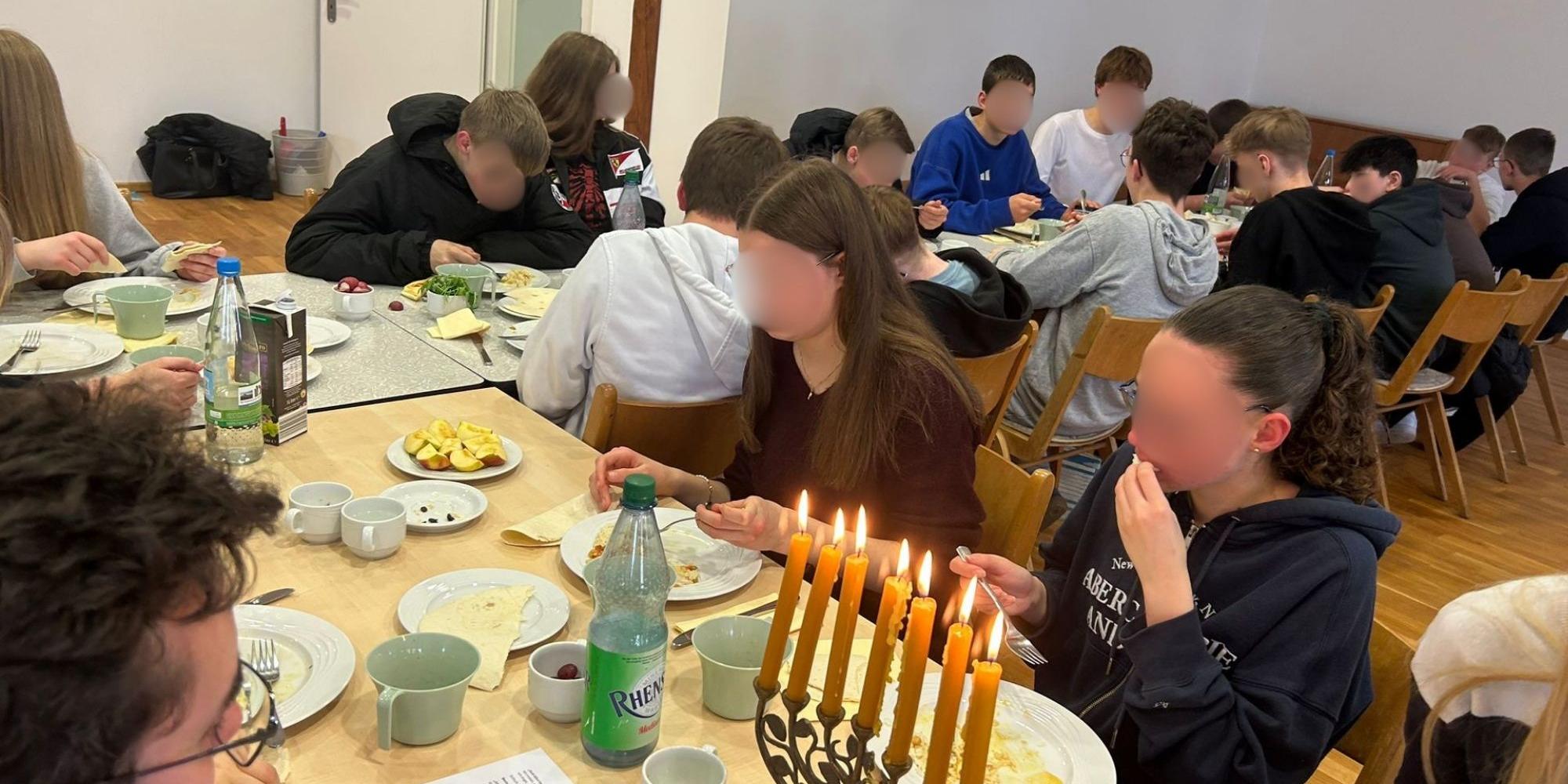 Menschen sitzen an einem gedeckten Tisch. Eine Menorah steht auf dem Tisch.
