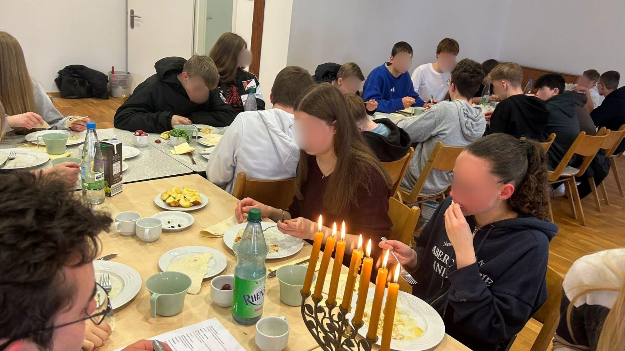 Menschen sitzen an einem gedeckten Tisch. Eine Menorah steht auf dem Tisch.