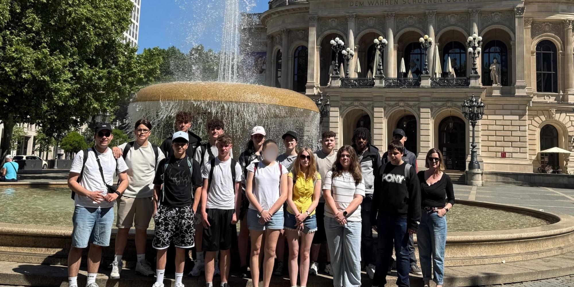 Gruppe von Jugendlichen vor einem Brunnen auf einem Platz in Frankfurt mit der Alten Oper im Hintergrund.