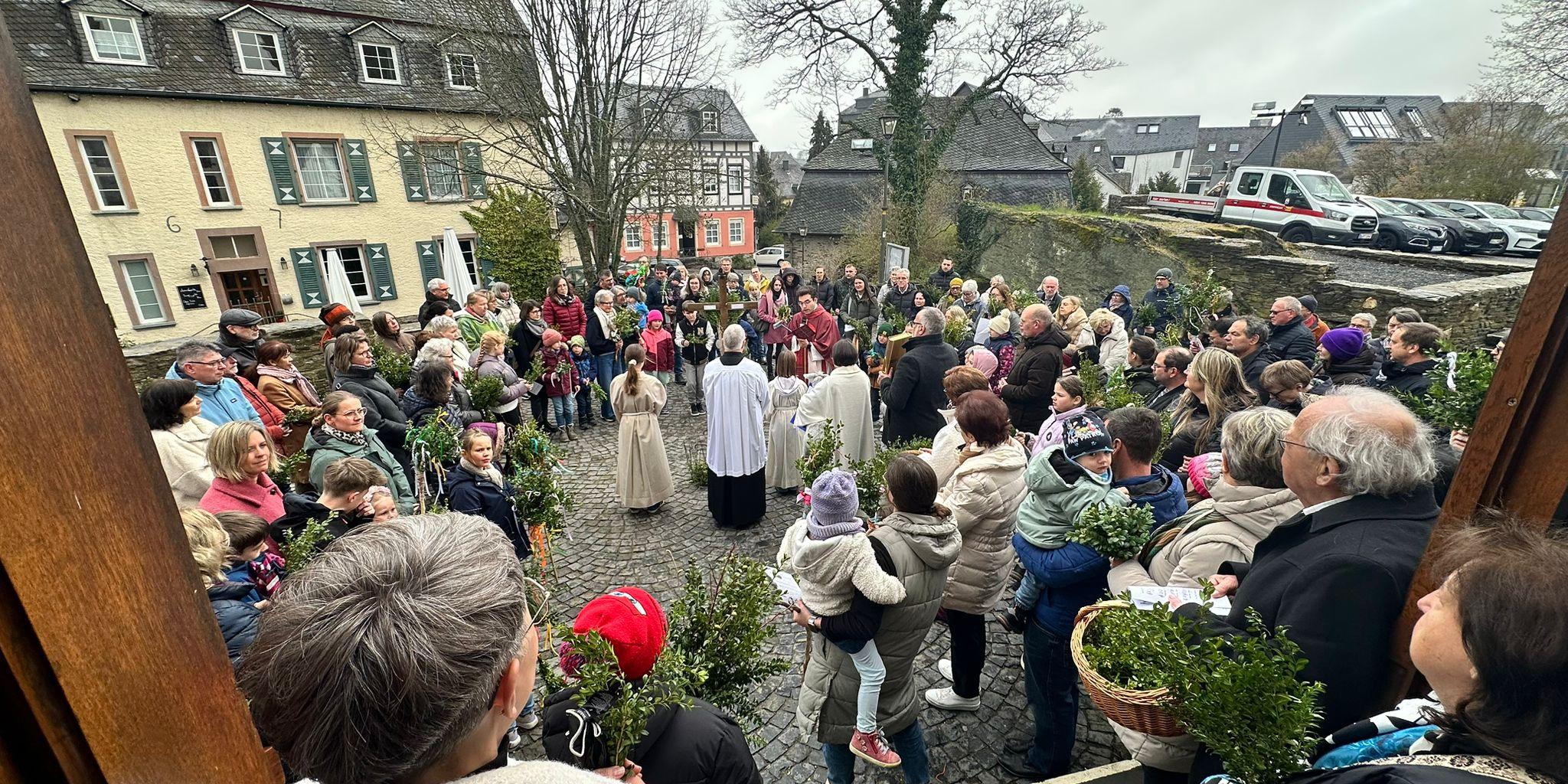 Die Gemeinde ist zur Palmweihe auf dem Kirchenvorplatz versammelt.