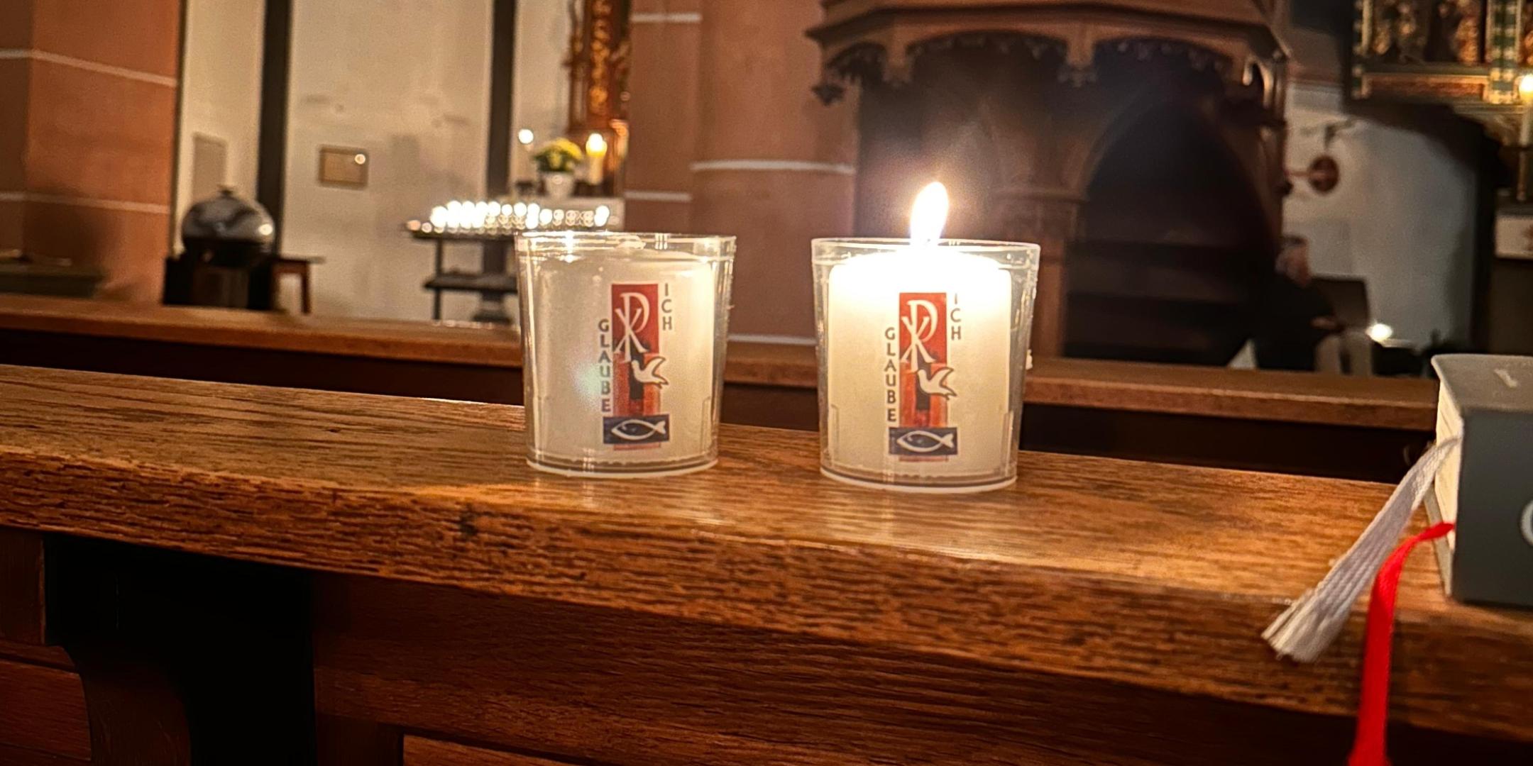 Kleine Osterkerzen brennen auf einer Kirchenbank.