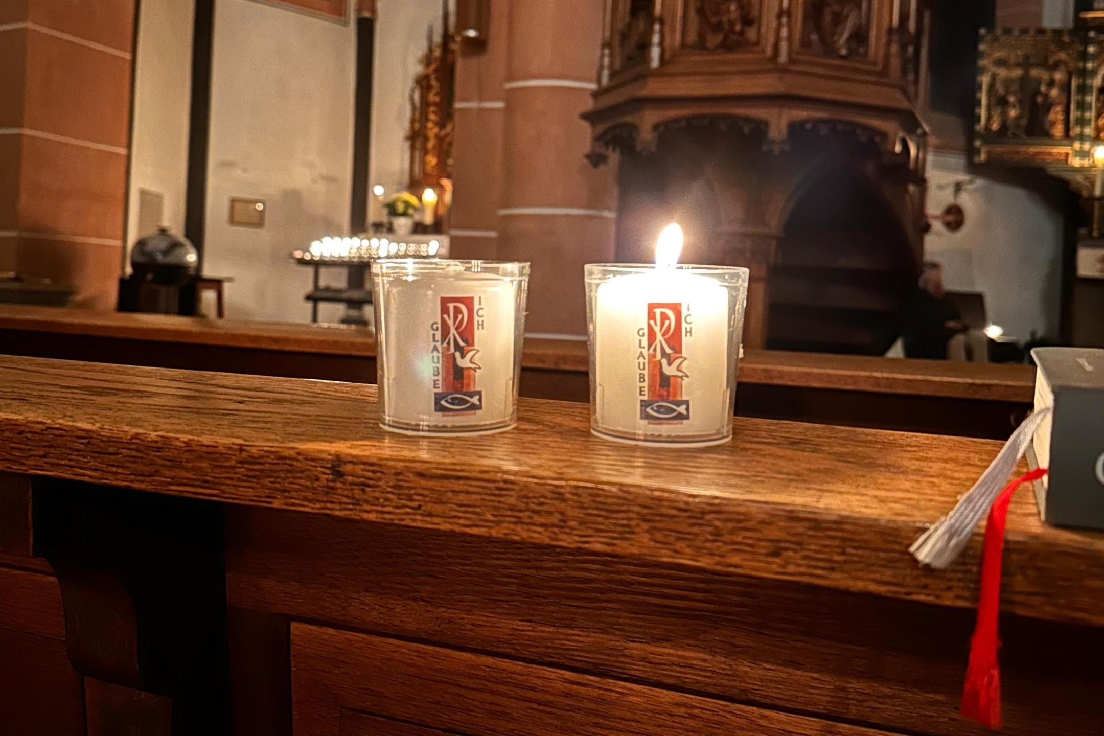 Kleine Osterkerzen brennen auf einer Kirchenbank.
