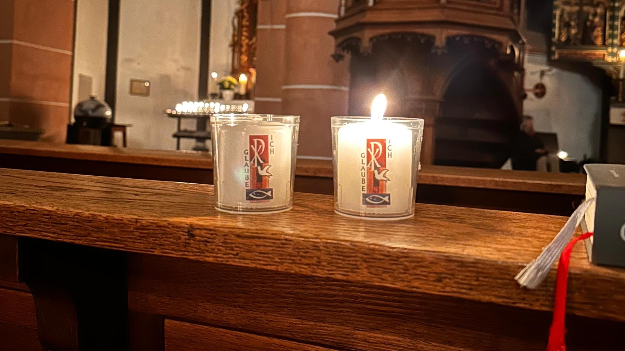 Kleine Osterkerzen brennen auf einer Kirchenbank.