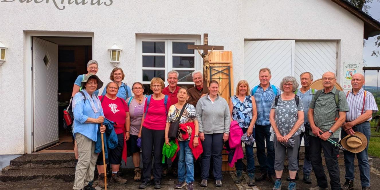 Personengruppe mit Kreuz vor einem Haus