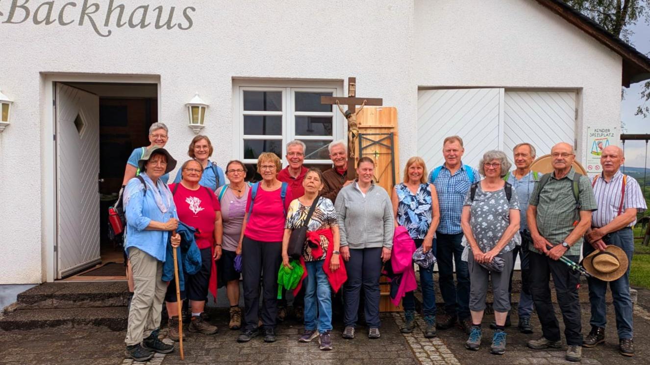 Personengruppe mit Kreuz vor einem Haus