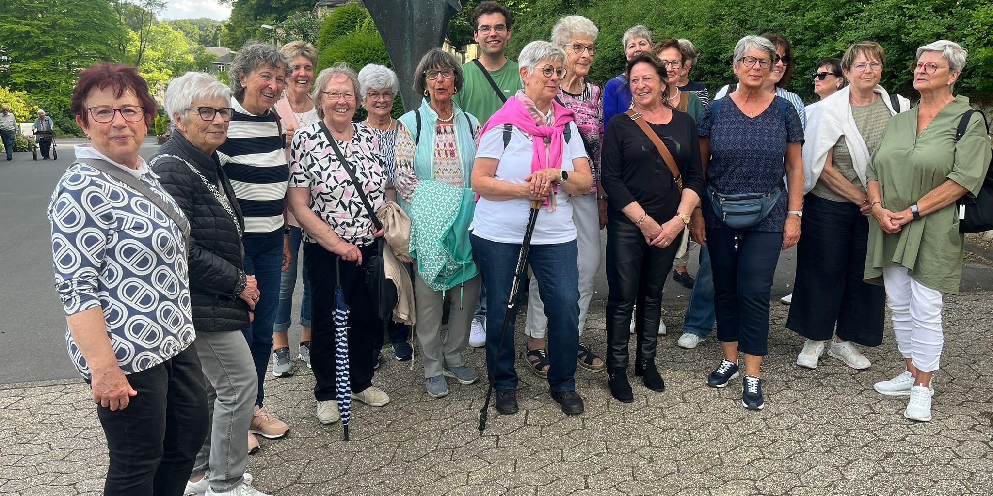 Eine größere Gruppe von Personen steht im Freien auf einem gepflasterten Weg zusammen. Hinter der Gruppe befindet sich eine große, dunkel gefärbte Skulptur mit ausgebreiteten Formen. Die Gruppe ist dicht nebeneinander aufgestellt und blickt in Richtung Kamera. Im Hintergrund sind Bäume und Grünflächen zu sehen, die den Ort als Teil des Klostergeländes erkennen lassen. Die Szene wirkt wie ein gemeinsames Erinnerungsfoto während des Ausflugs. (c) Dorothee Ullmann Eine größere Gruppe von Personen steht im Freien auf einem gepflasterten Weg zusammen. Hinter der Gruppe befindet sich eine große, dunkel gefärbte Skulptur mit ausgebreiteten Formen. Die Gruppe ist dicht nebeneinander aufgestellt und blickt in Richtung Kamera. Im Hintergrund sind Bäume und Grünflächen zu sehen, die den Ort als Teil des Klostergeländes erkennen lassen. Die Szene wirkt wie ein gemeinsames Erinnerungsfoto während des Ausflugs.