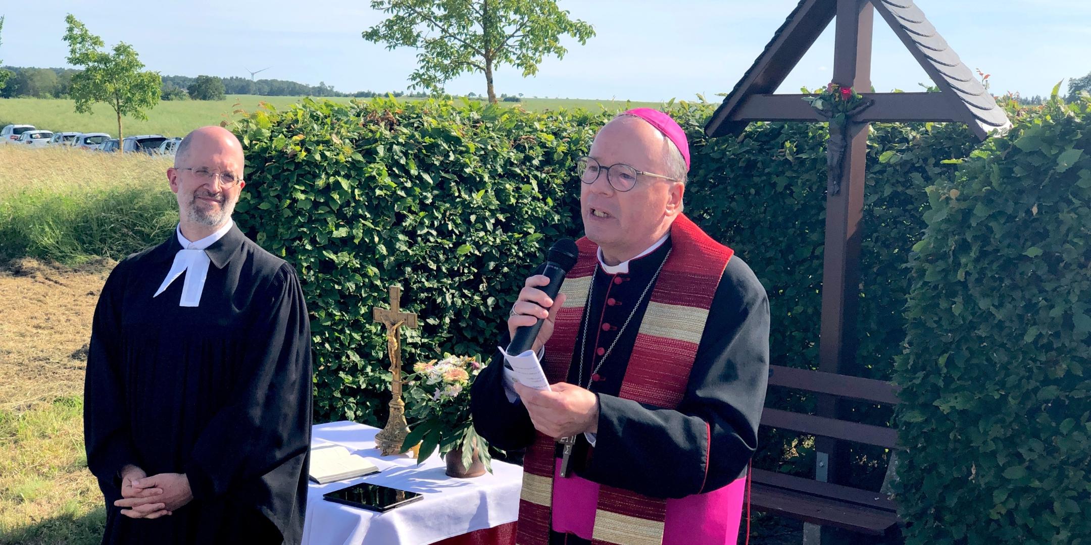 evangelischer und katholischer Geistlicher im Gespräch vor einem Kreuz und einer Hecke (c) Dieter Junker evangelischer und katholischer Geistlicher im Gespräch vor einem Kreuz und einer Hecke