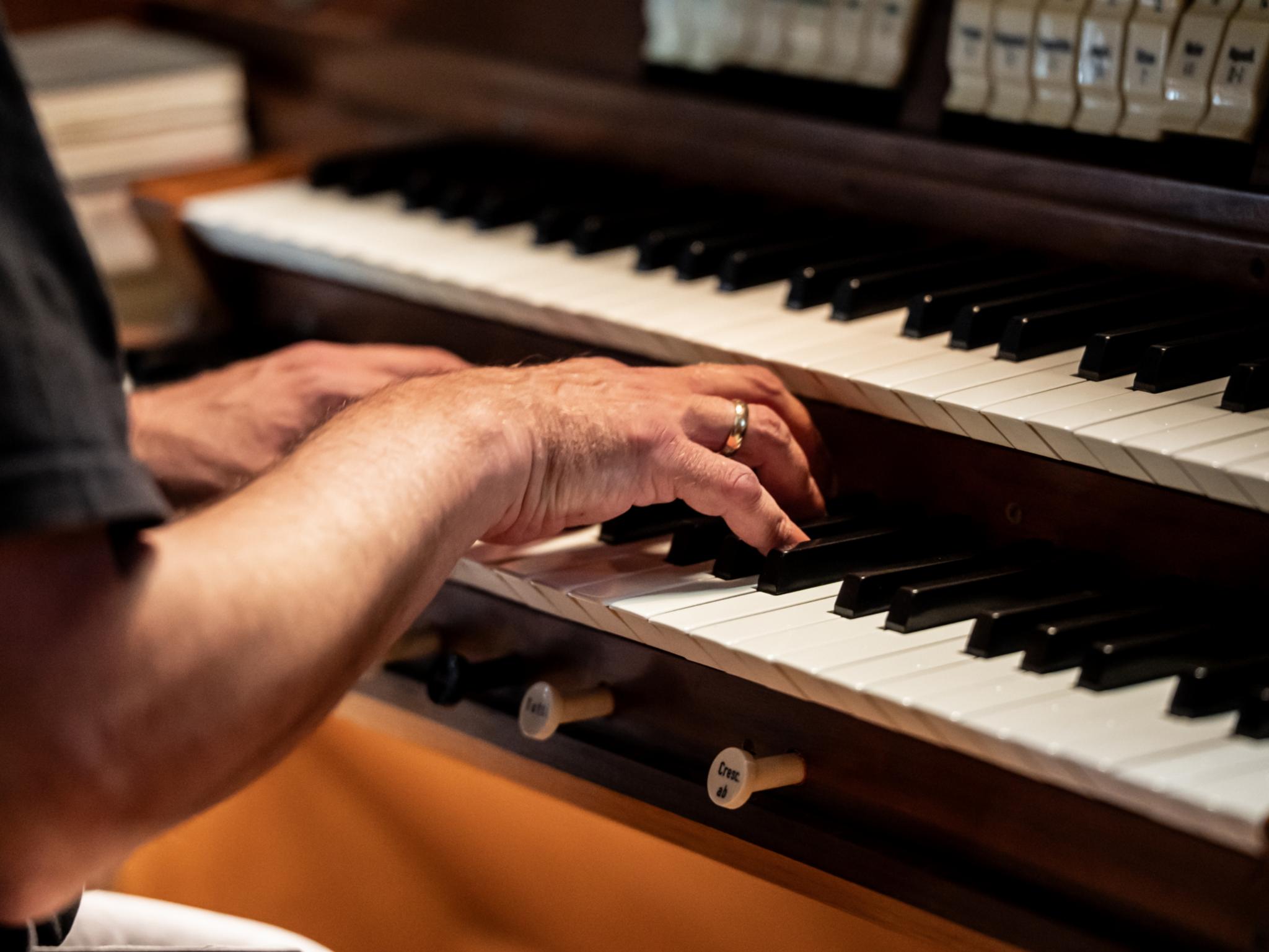 Hände spielen auf den Manualen einer Kirchenorgel. Die Aufnahme zeigt die musikalische Begleitung eines Gottesdienstes durch die Orgel.