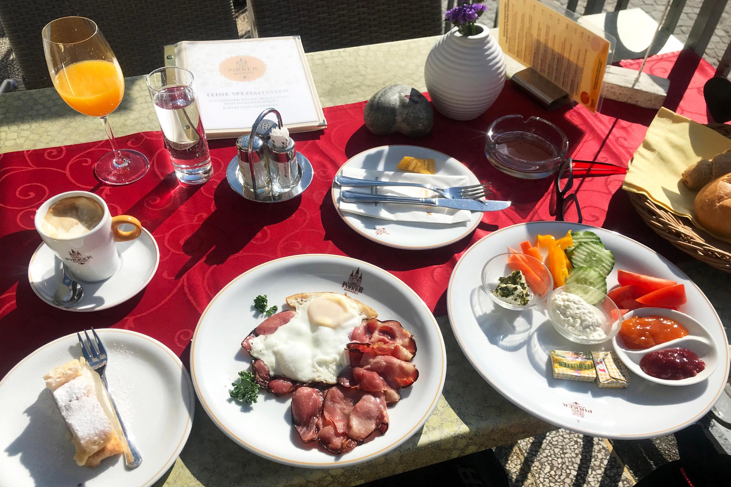 mehrere Frühstücksteller mit Speisen , dazu Saftglas und Kaffeetasse